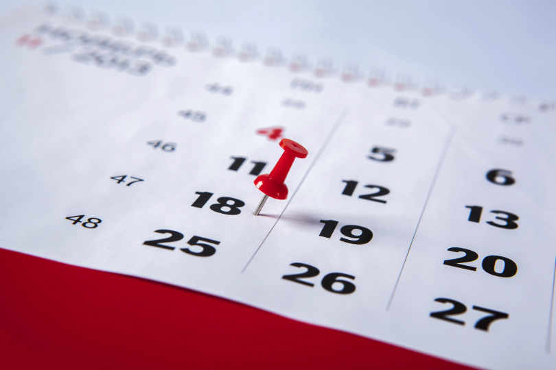Calendário com datas impressas na cor preta. Há um alfinete vermelho marcando o dia 18.