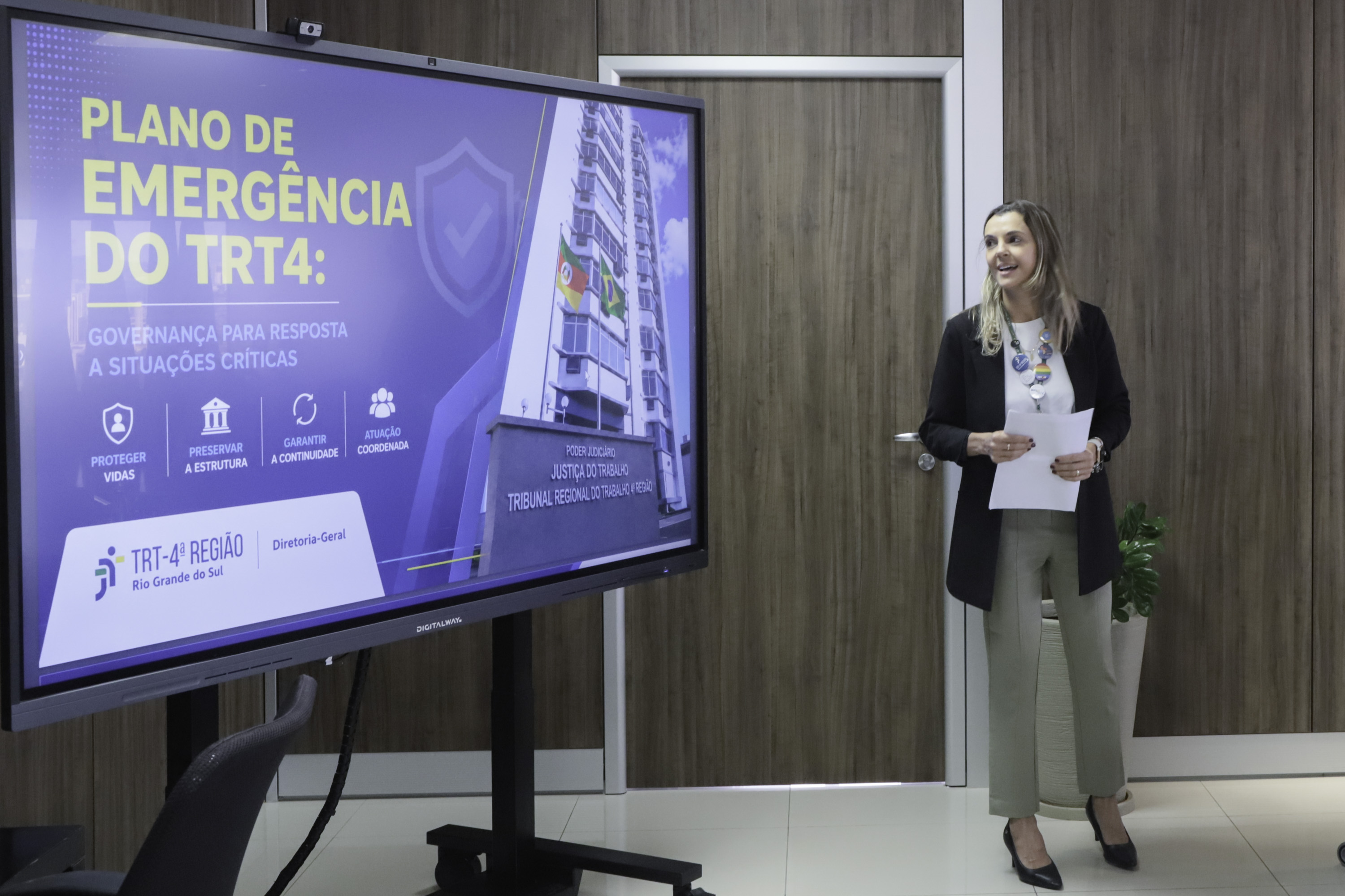 Tela na esquerda exibe arte do Plano, Ana Paula aparece de pé na direita sorrindo.