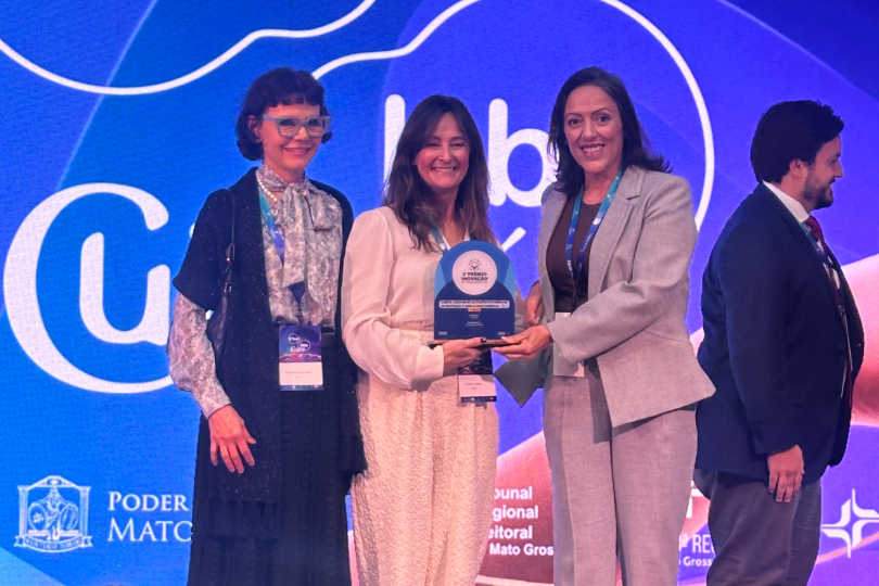 Três mulheres recebem a premiação. Ao fundo, há um painel azul com a inscrição em branco: 6º FestLabs - Cuiabá, 2026