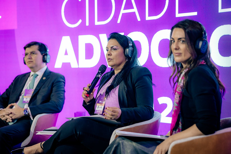 Desa. Tânia Reckziegel falando ao microfone, durante o painel, ao lado dos outros painelistas
