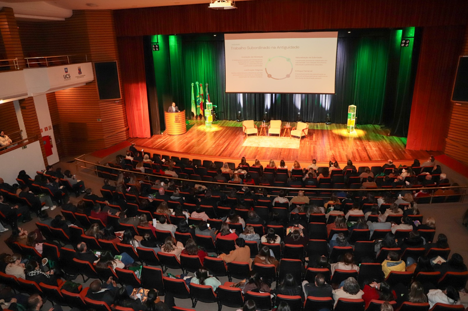 A Foto de cima mostra auditório com público e palestrante embaixo.