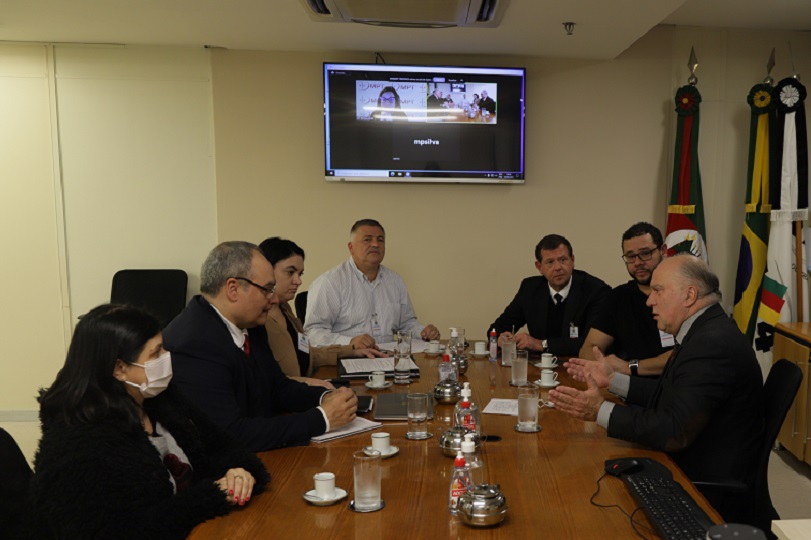 Participantes da audiência de mediação. Parte dos integrantes estão sentados ao redor da mesa, nas dependências do TRT-4, e parte está acompanhando por videoconferência. 
