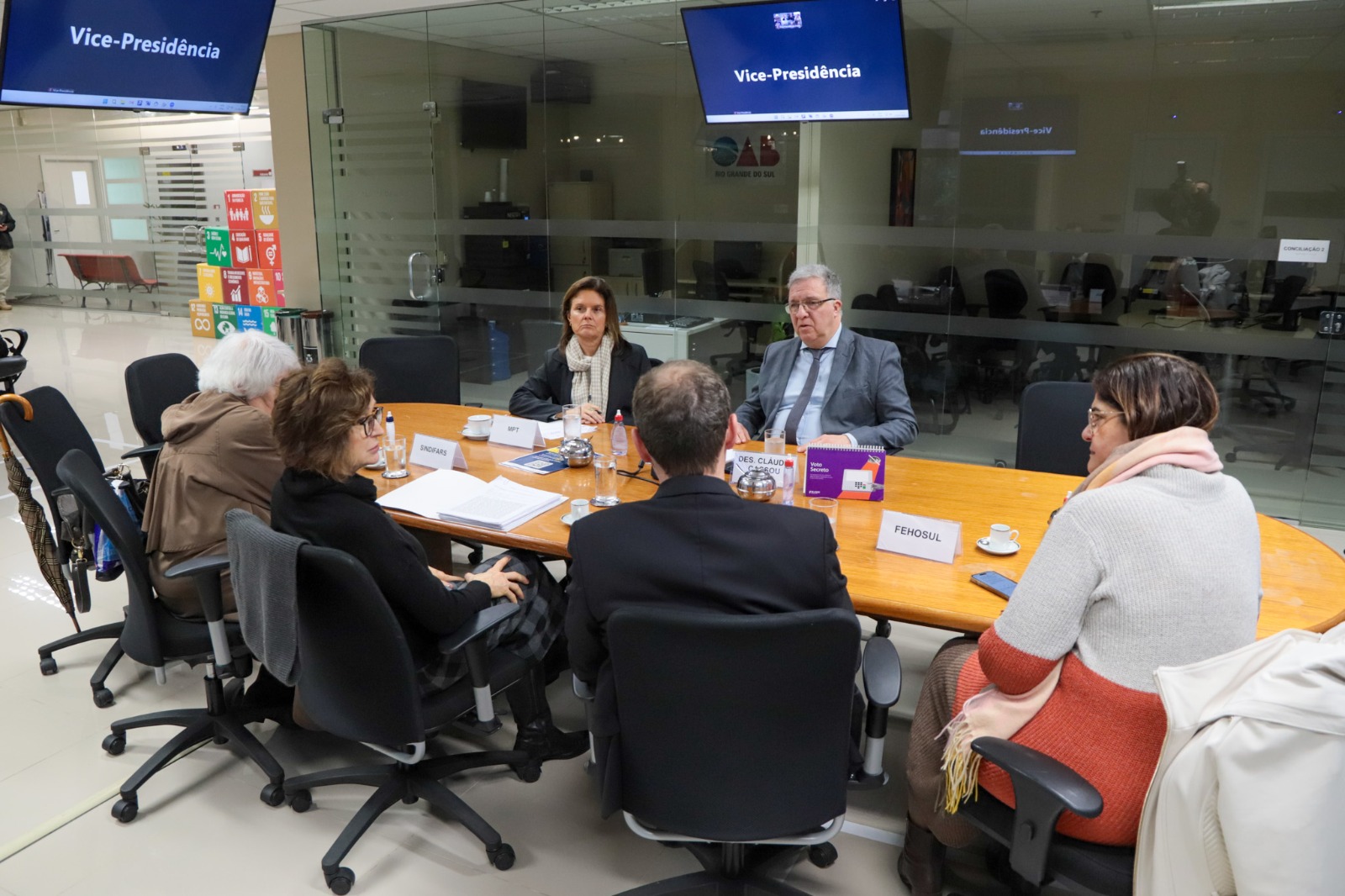 A foto mostra mesa de mediação com as partes com telas escrito vice-presidência de fundo.