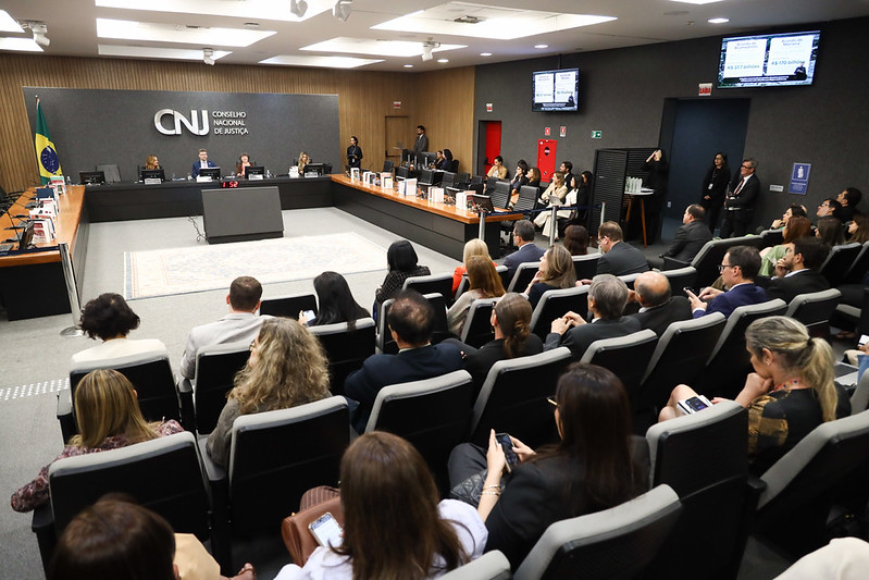 Foto em ângulo aberto, mostrando mesa oficial e público presente