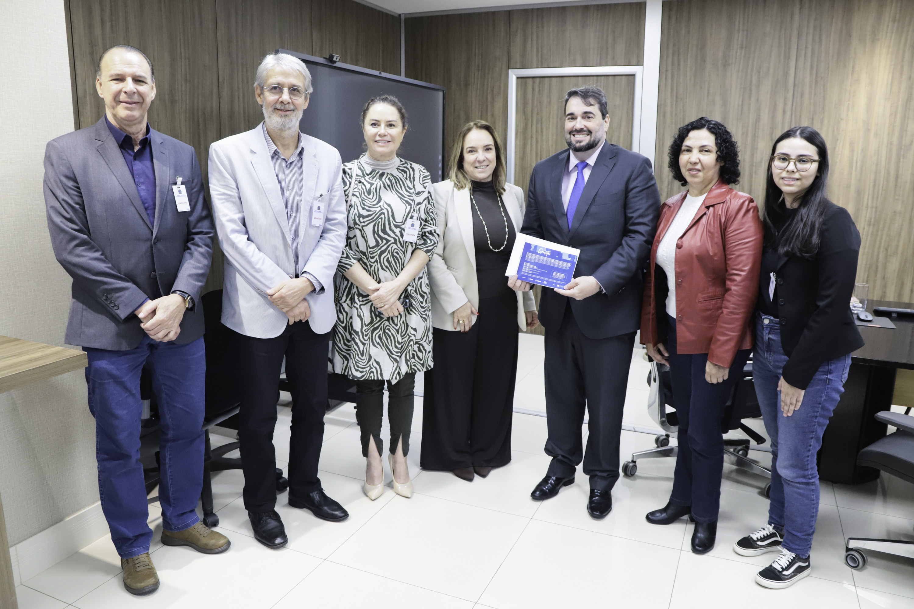 sete pessoas posam sorrindo para  foto. o presidente está ao centro segurando um convite. 