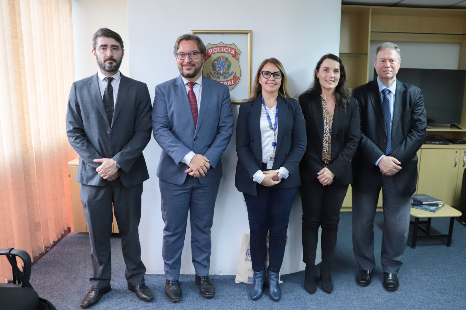 Cinco pessoas posam para a foto, com um quadro com o brasão da Polícia Federal na parede.