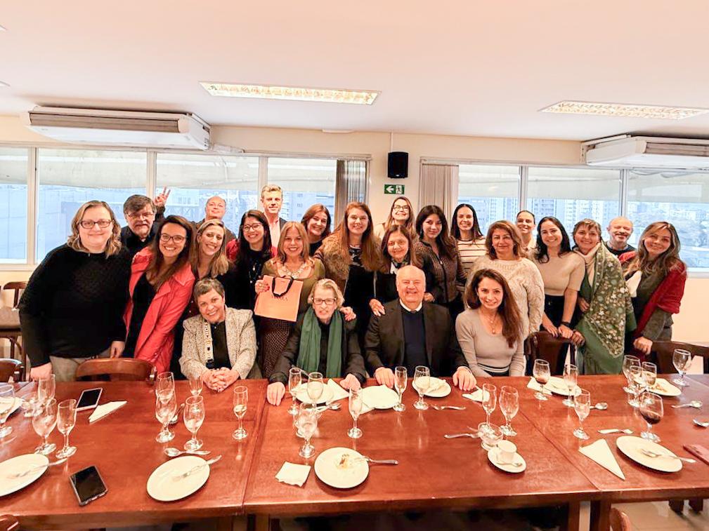 diversos participantes da homenagem posam para a foto, atrás de uma grande mesa. 