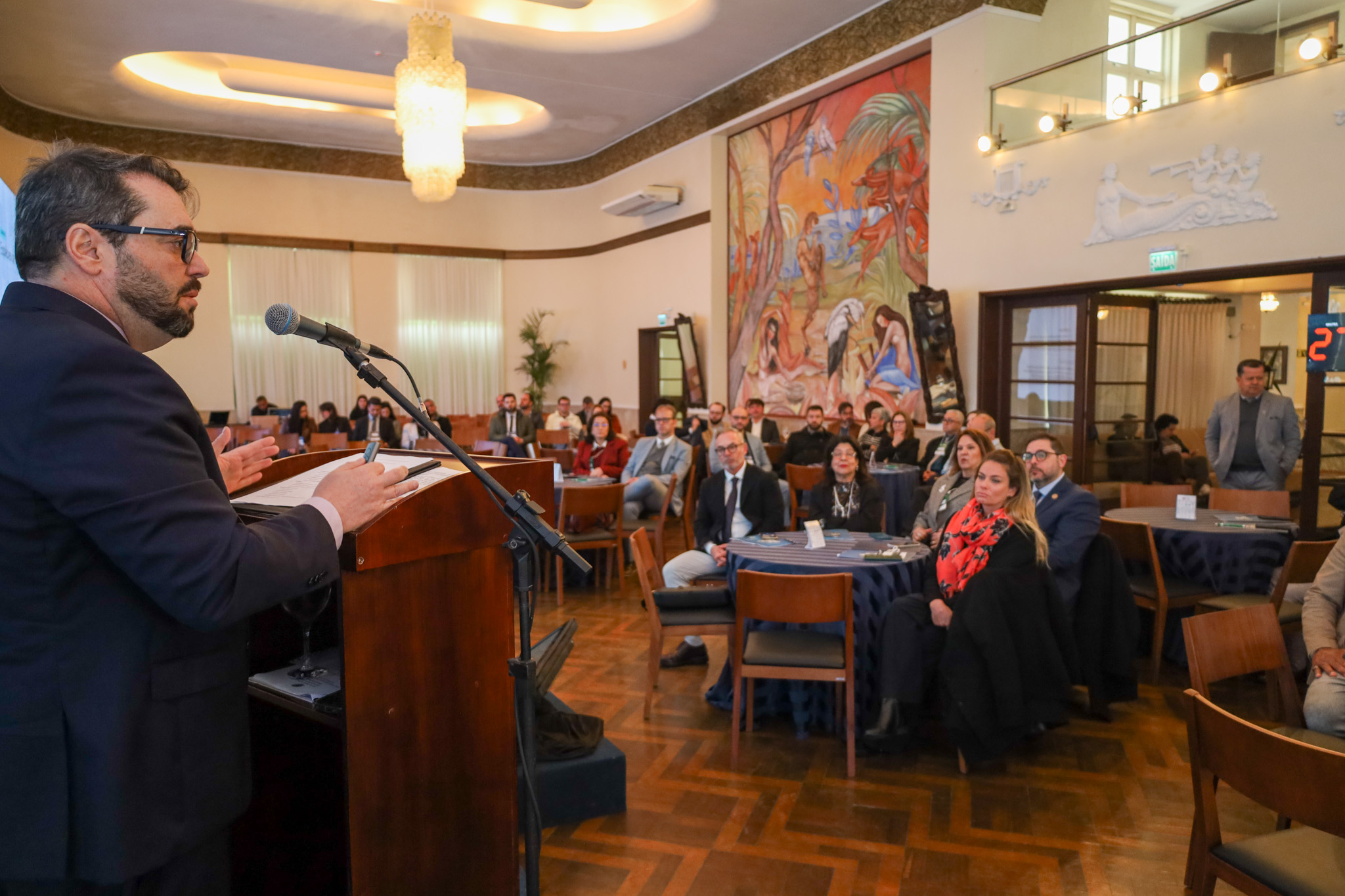 Des. Alexandre falando ao microfone. Ao fundo, o público assistindo.