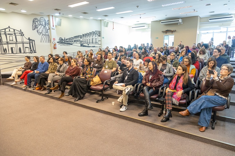A fotografia mostra a plateia com o auditório praticamente lotado.