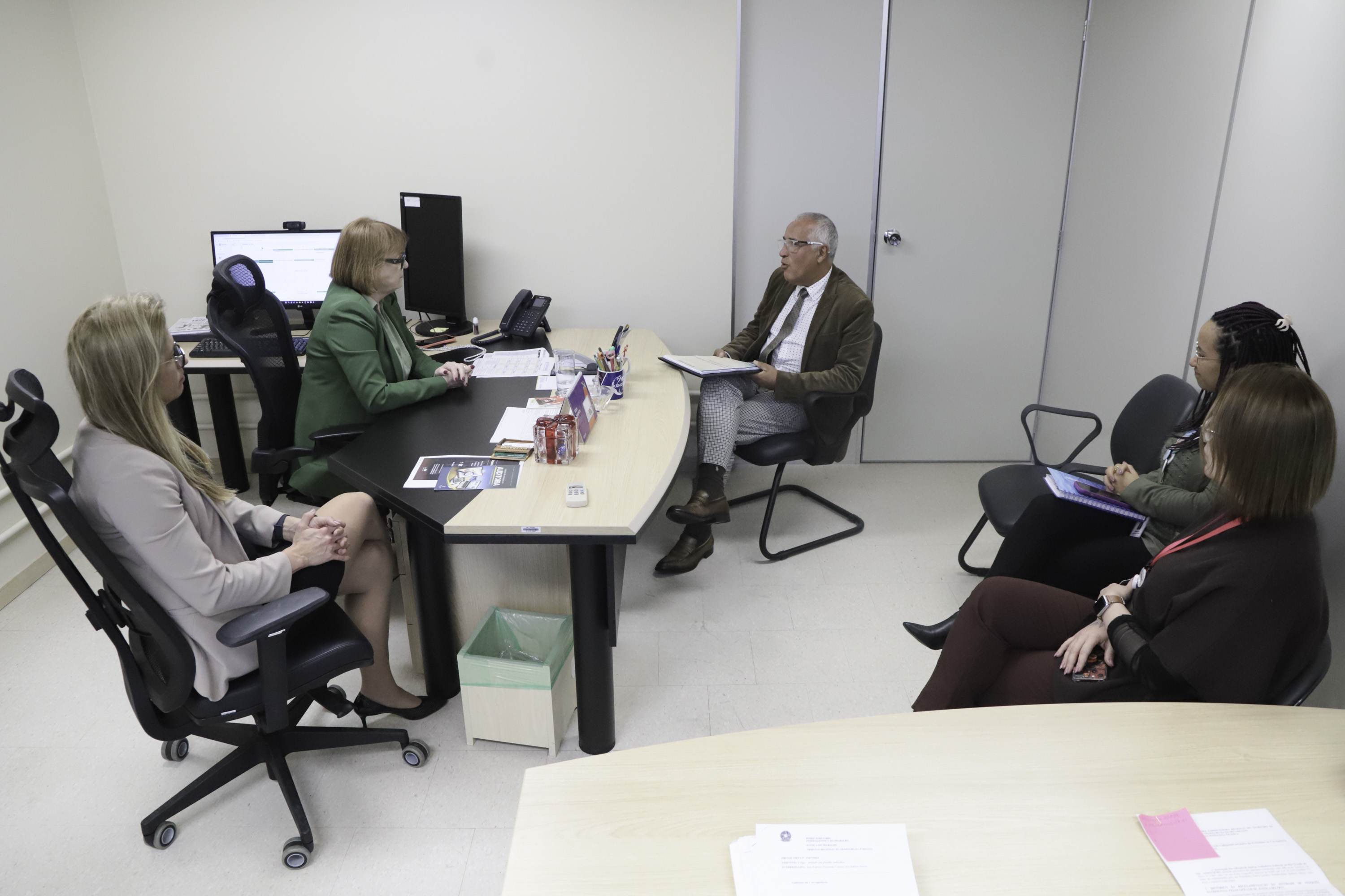 participantes da reunião aparecem sentados na sala. Ao centro, Gilberto está segurando o plano e falando. 