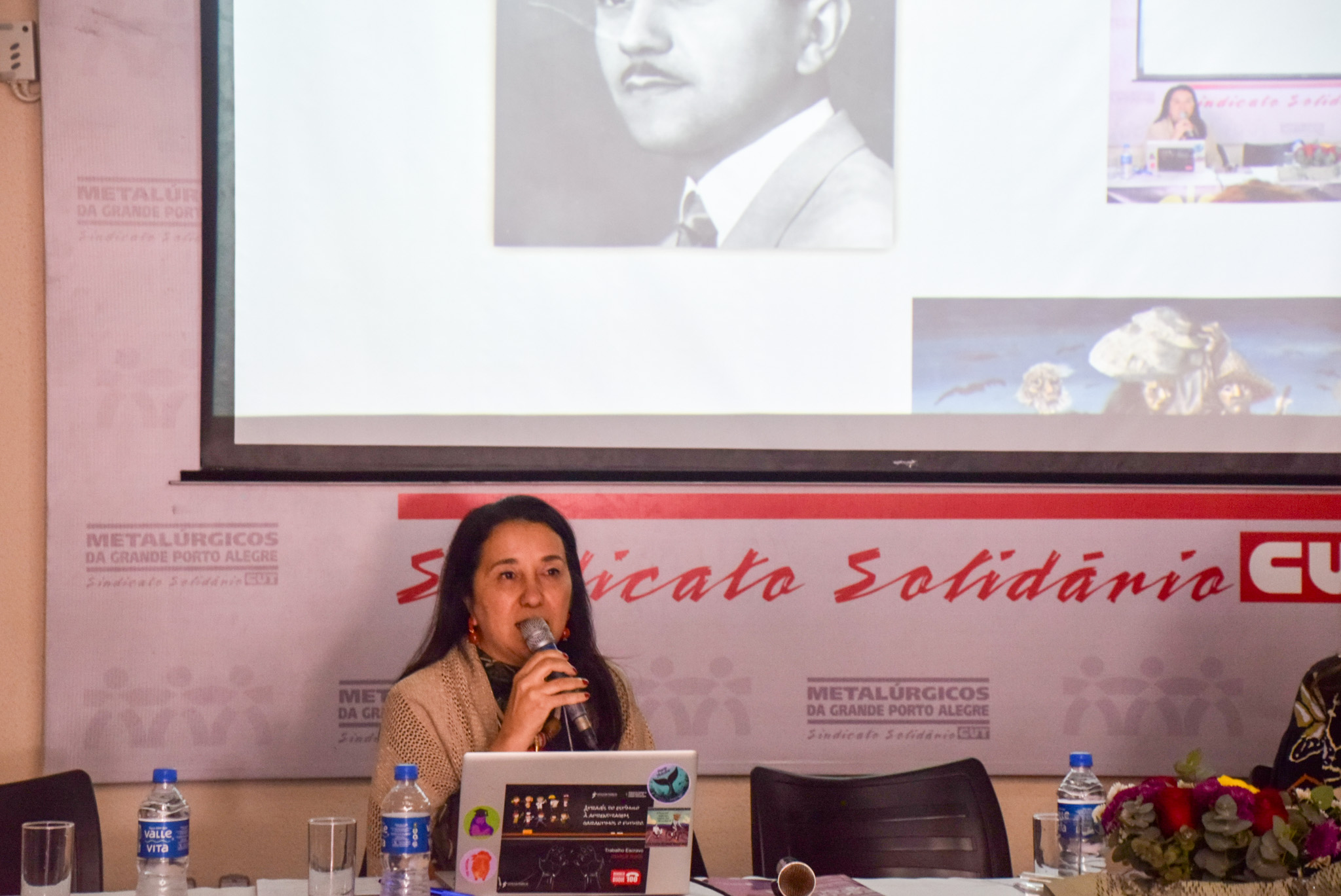 A foto mostra a juíza Maria Teresa falando ao microfone.