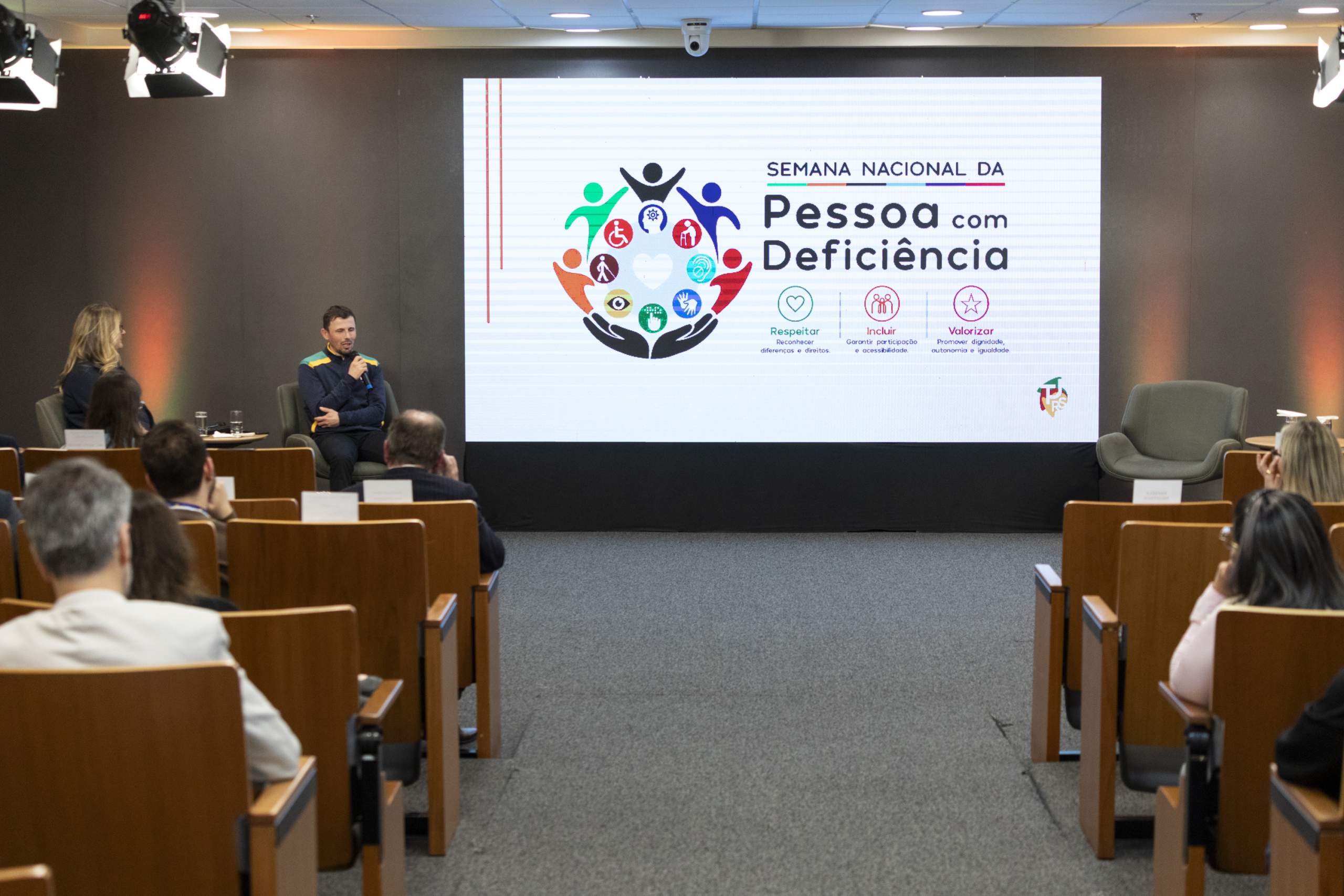 Foto do Ricardo palestrando e o público assistindo.