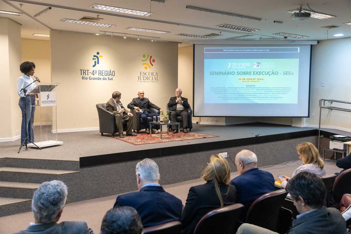 Palco do evento com mestre de cerimônias e palestrantes do painel de abertura.