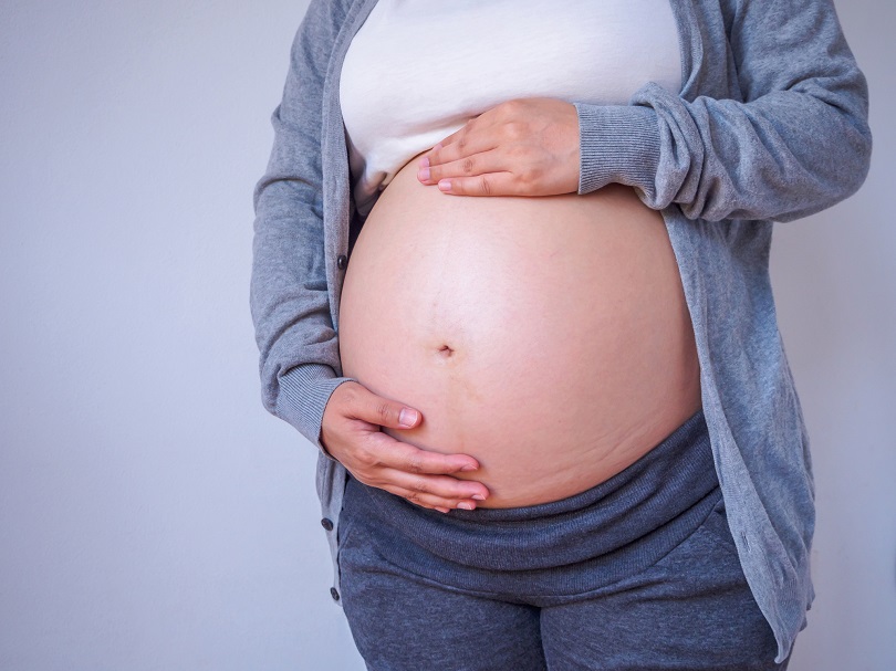 Foto ilustrativa de mulher grávida com as mãos em torno da barriga. 