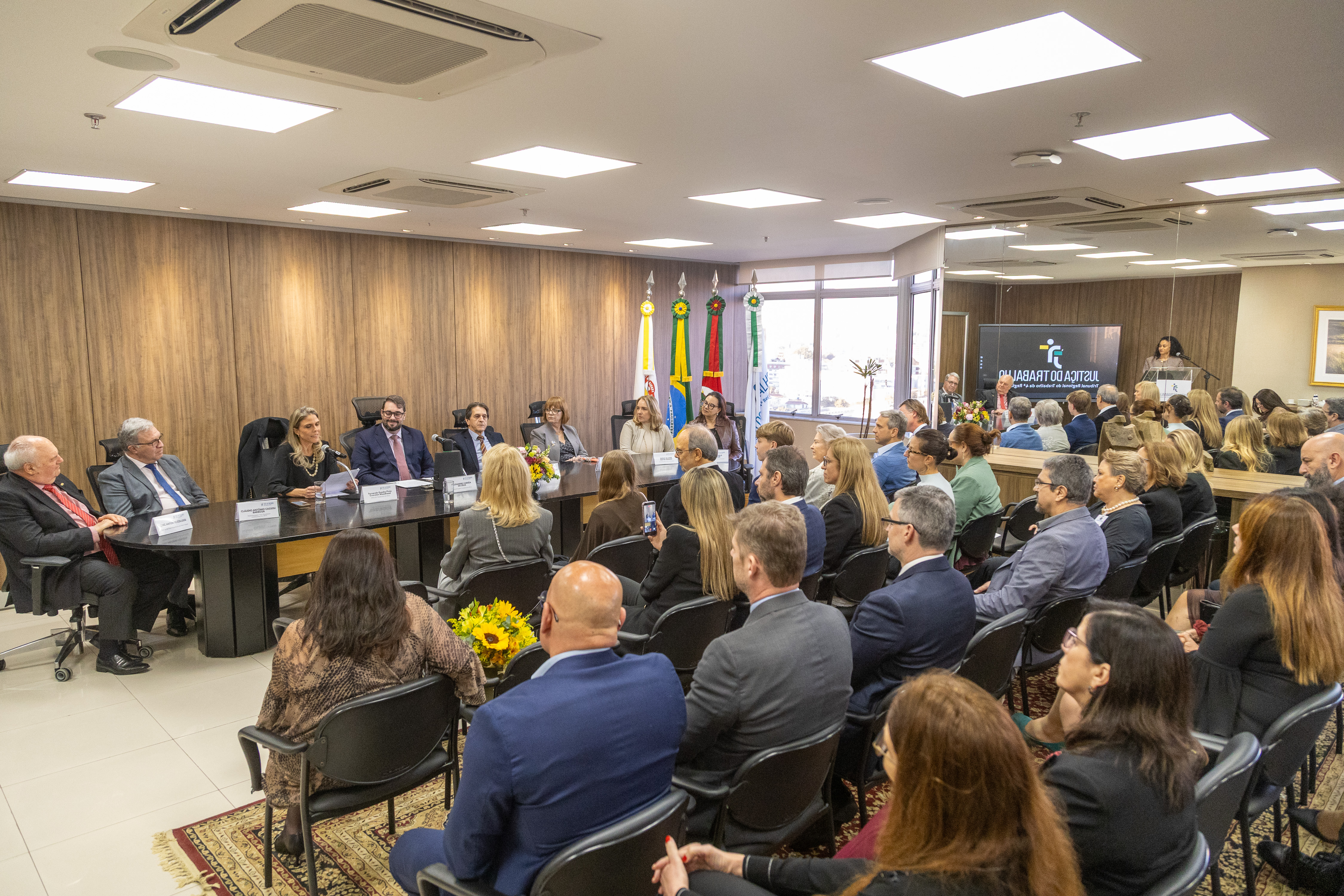 Foto em ângulo aberto, mostrando público e mesa oficial