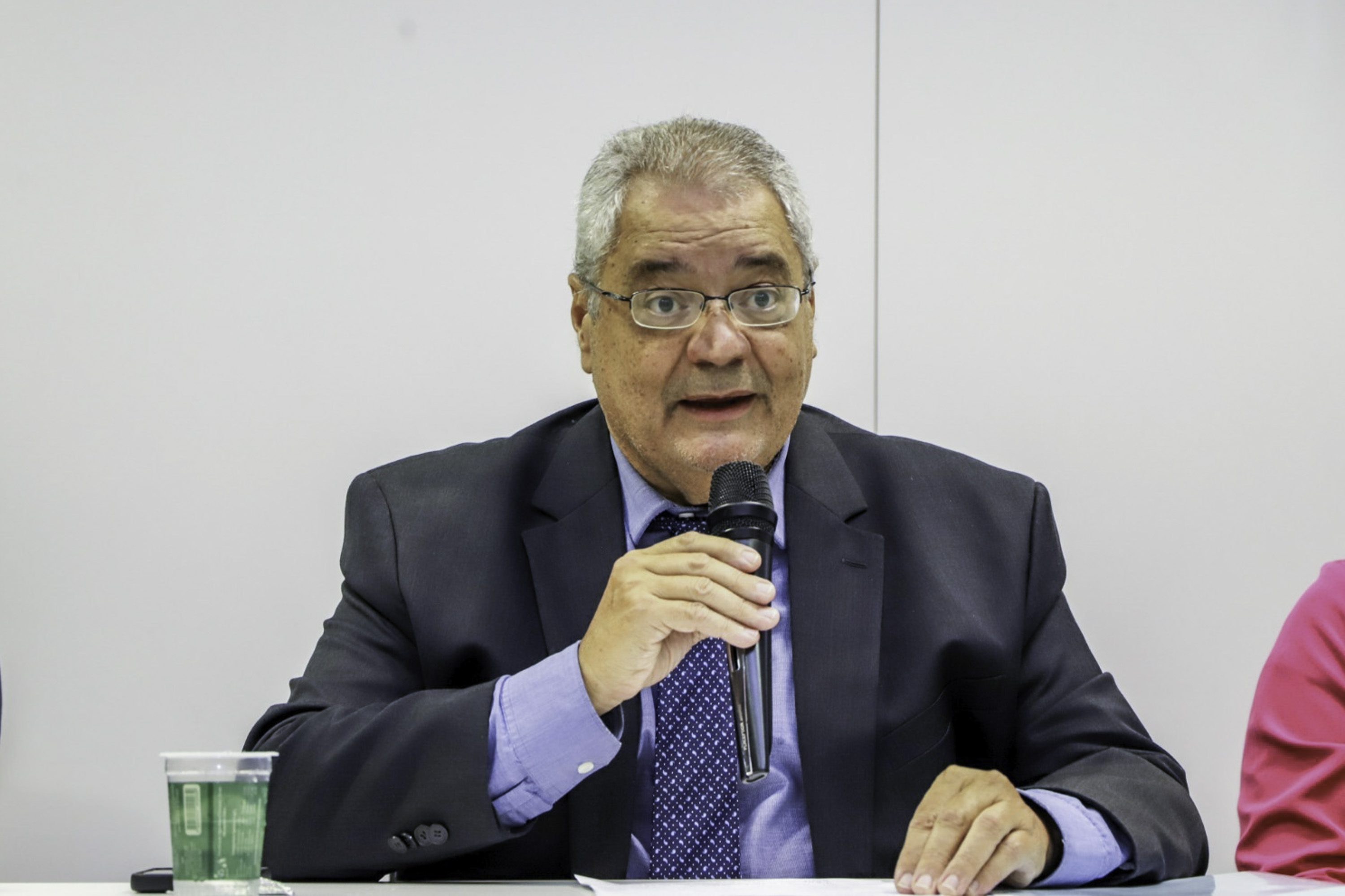 Cassal fala ao microfone em uma mesa oficial de evento. 