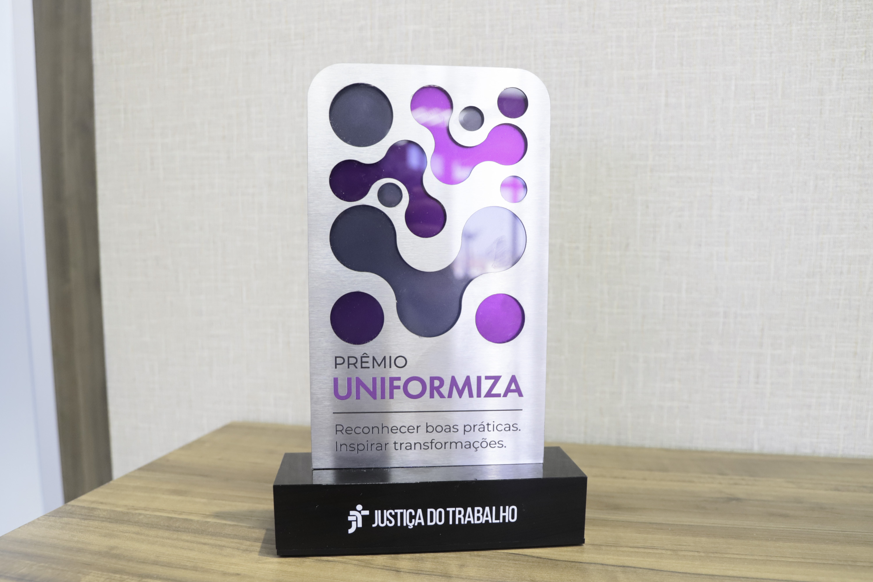 Troféu da premiação com a arte nas cres roxo e cinza. 