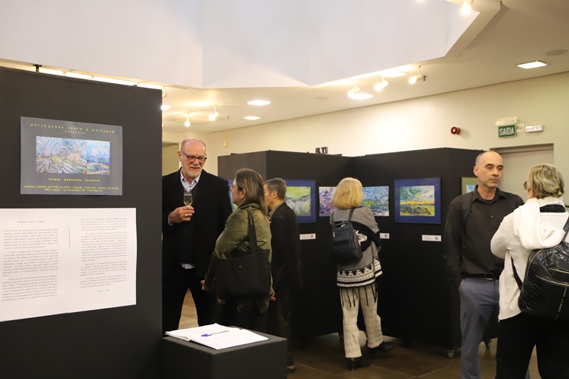Imagem da exposição. Na foto aparecem pessoas conversando e observando os quadros.