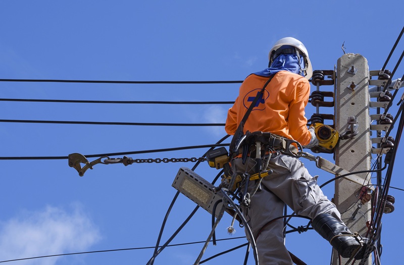 A fotografia mostra um trabalhador pendurado em um poste de energia.
