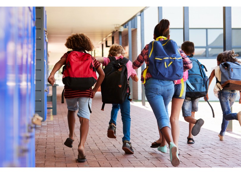 Crianças com mochilas caminhando juntas em direção à escola.