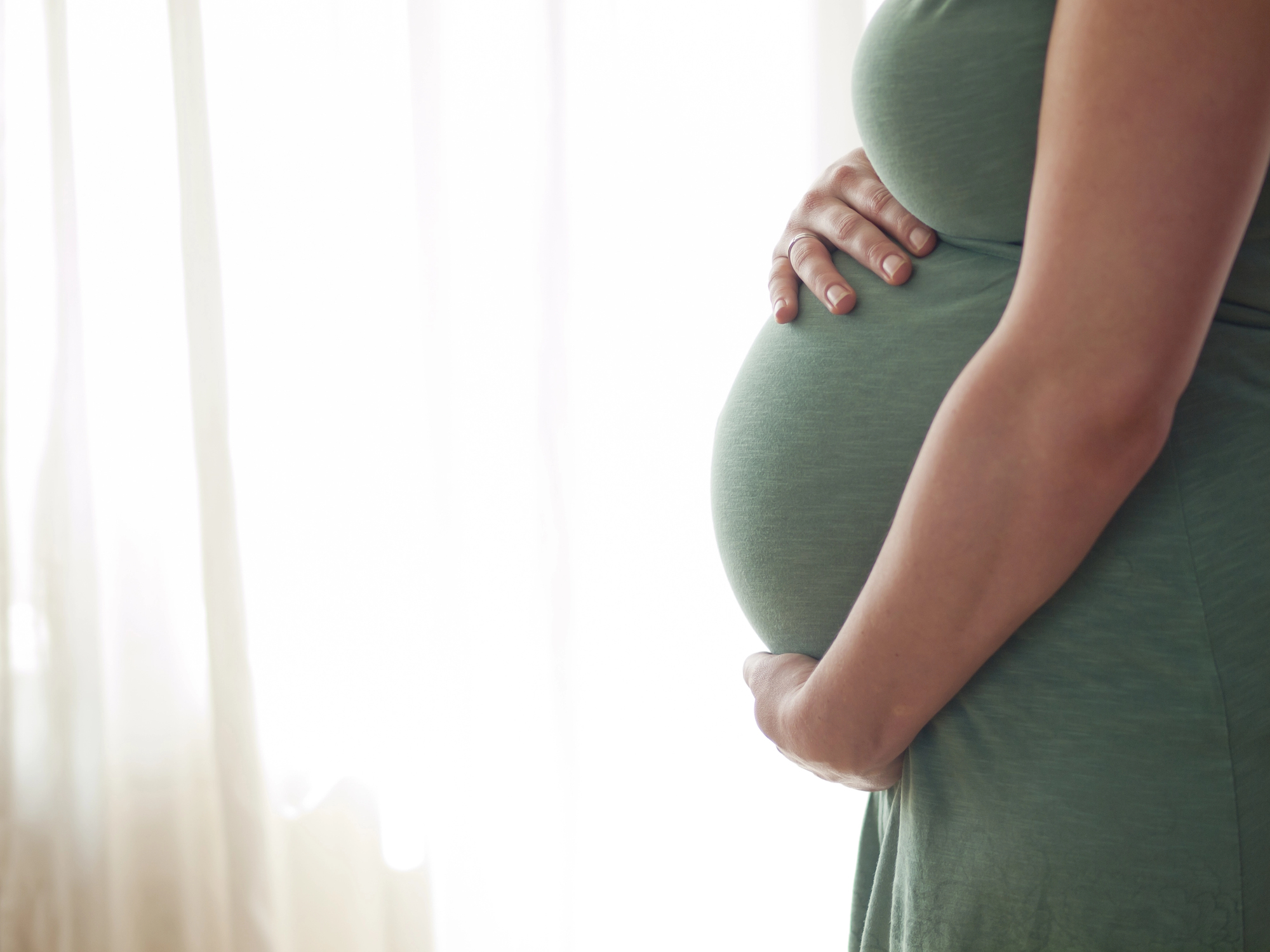 A foto mostra uma mulher grávida segurando a barriga.
