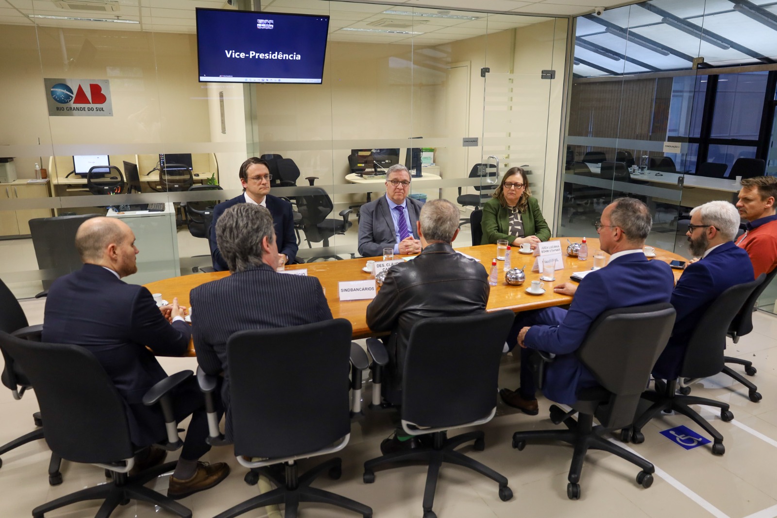 A foto mostra mesa com várias pessoas ao redor dela sentadas conversando.