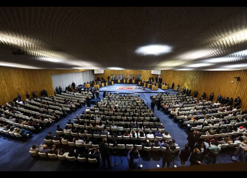 Foto tirada de um ângulo alto do Plenário, mostrando as pessoas assistindo e outras nas mesas.