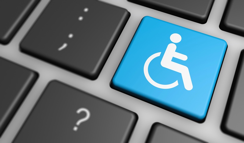 A imagem é o close em um teclado de computador, sendo que uma das teclas tem o símbolo, em azul, de uma pessoa com deficiência, no caso, utilizando cadeira de rodas.