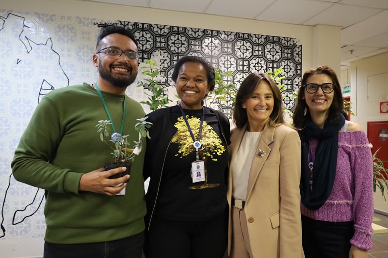Imagem de integrantes da Coordenadoria de Sustentabilidade, Acessibilidade e Inclusão e da juíza auxiliar Luciana Caringi. Cicero, Eliane, Luciana e Elen estão em pé sorrindo um ao lado do outro. Cicero segura um  vaso de planta.