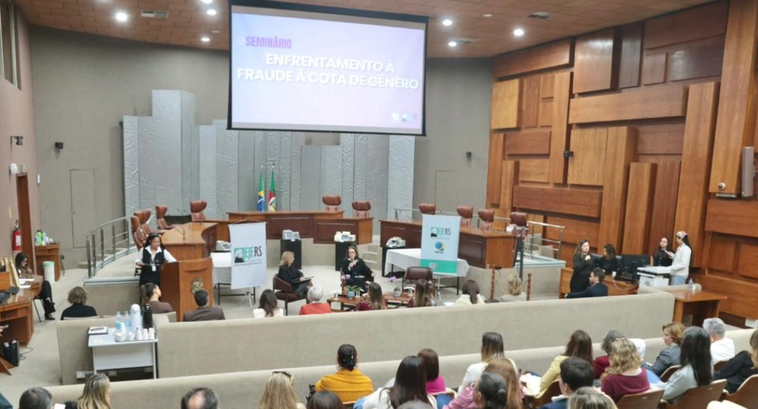 Foto das pessoas de costas, assistindo a duas mulheres no centro discursando.