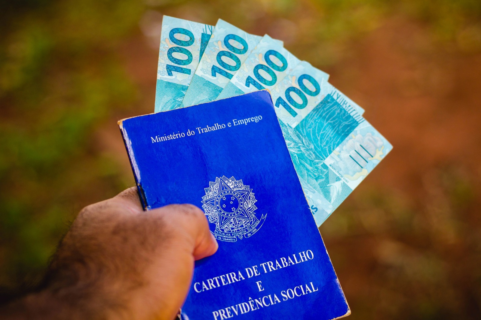 A foto mostra uma carteira de trabalho e três notas de cem reais
