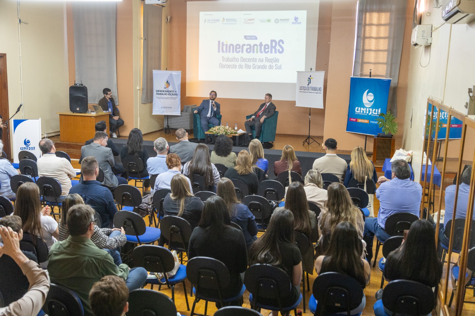 A foto mostra plano aberto auditório cheio.