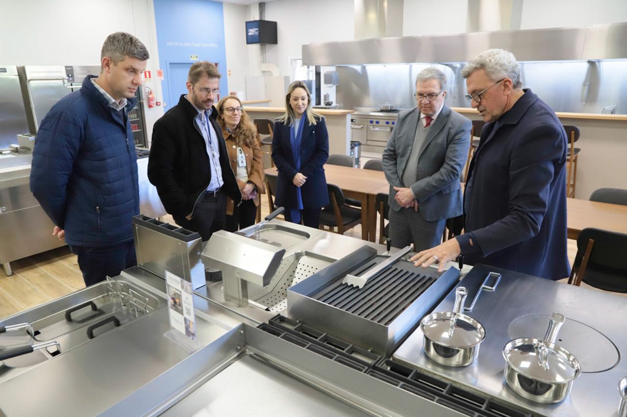 seis pessoas aparecem na foto olhando equipamentos de uma cozinha. 