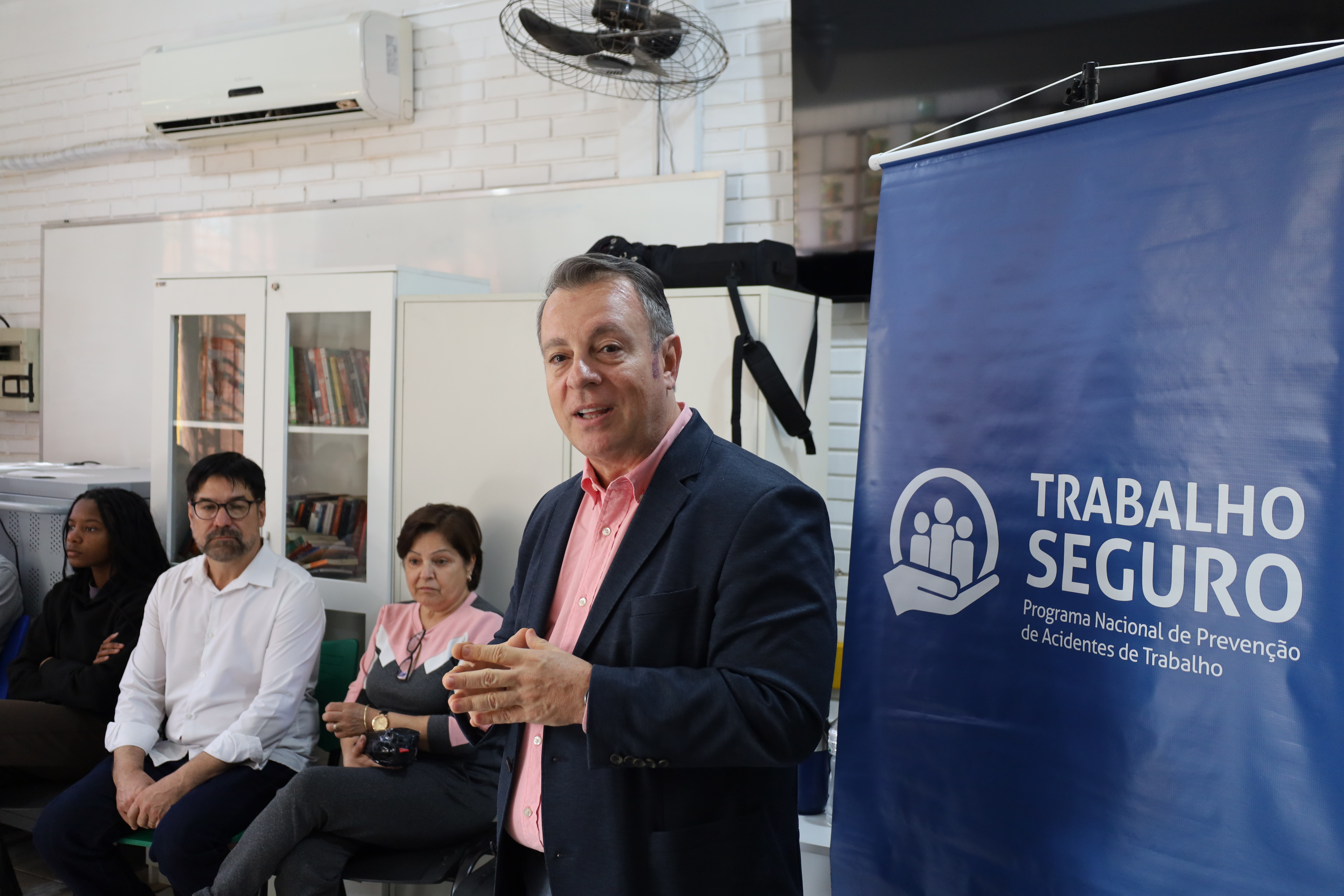 marcio falando, com um banner do lado escrito "trabalho seguro"