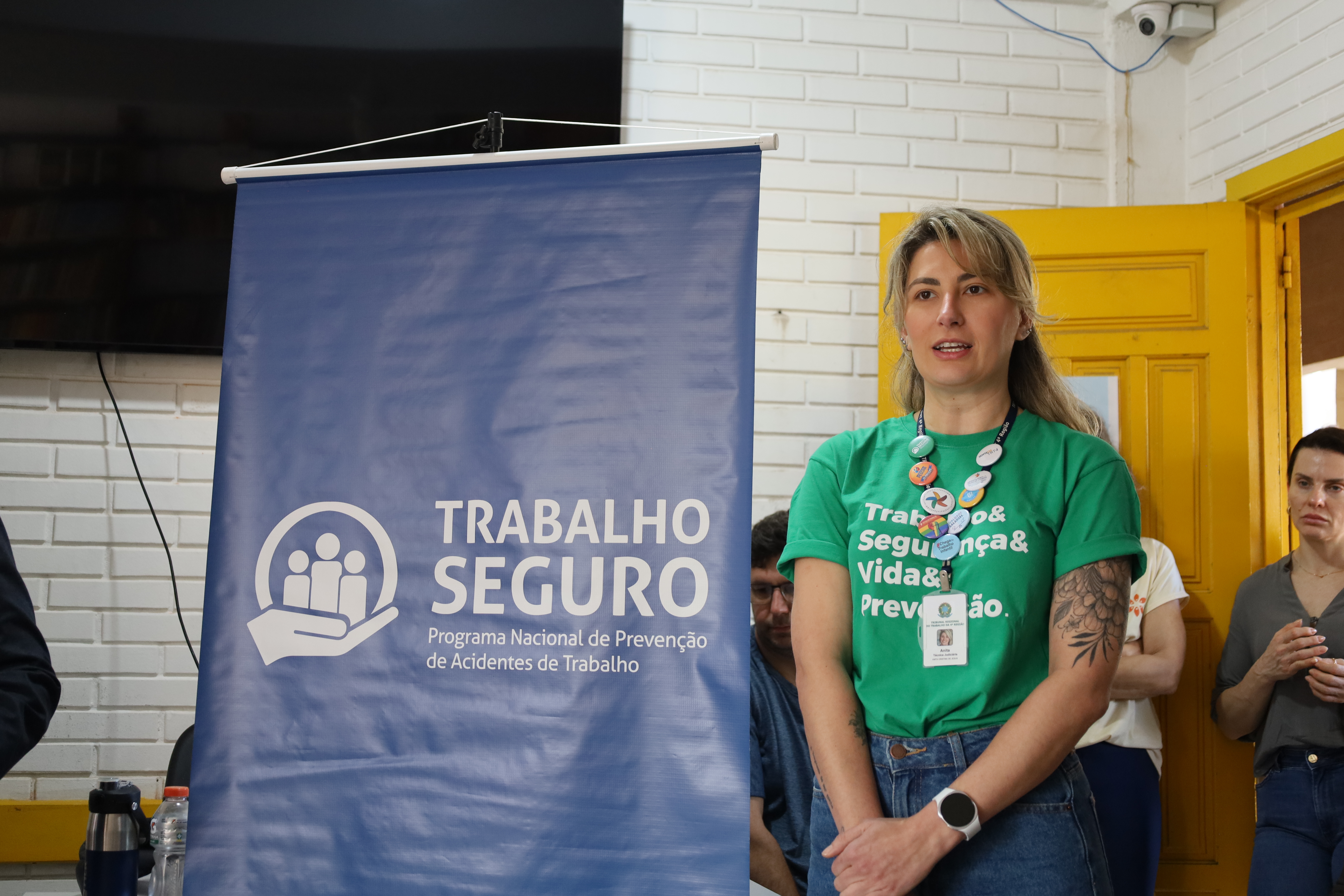 Anita falando, com um banner do lado escrito "Trabalho Seguro"