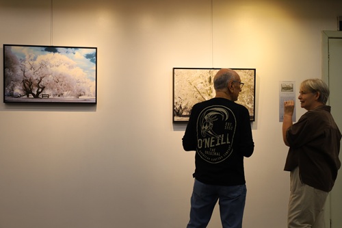 Imagem de duas pessoas conversando na frente das imagens da exposição.