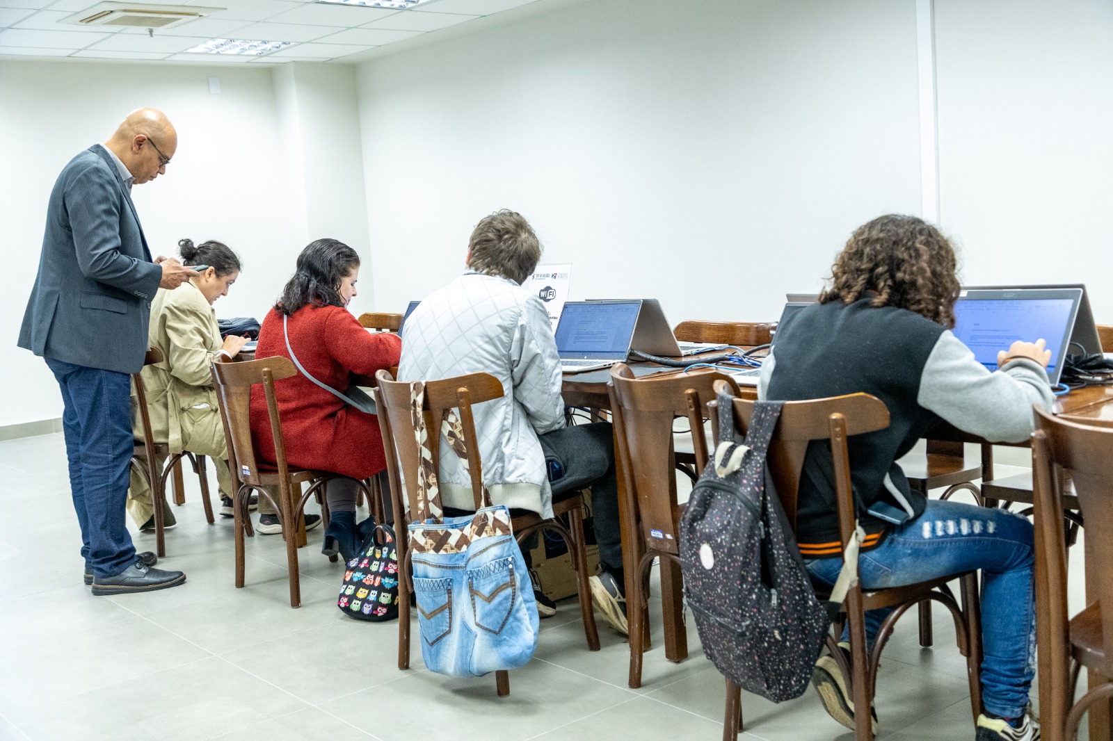 Ministrantes está de pé na esquerda, várias pessoas aparecem sentadas em mesas usando computadores