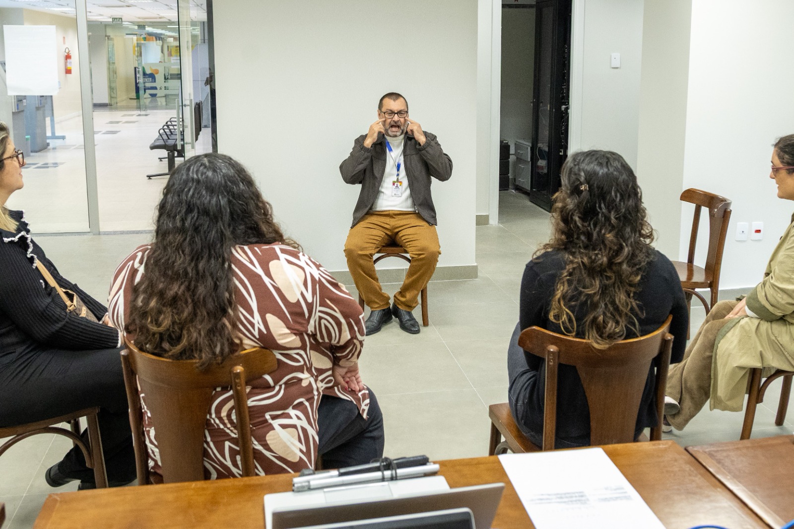 Ministrante aparece ao centro gesticulando sinais de libras, o público aparece sentado de costas.