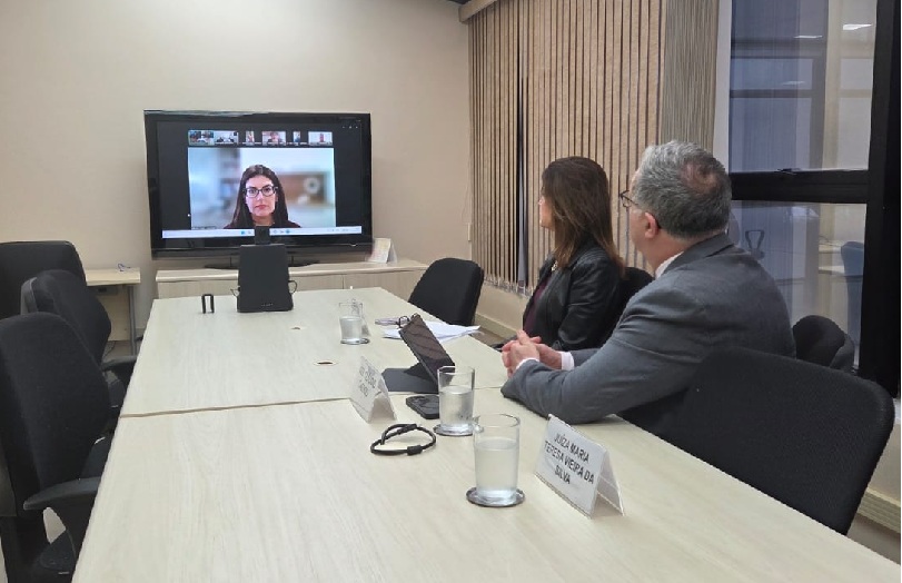 Foto da mediação, mostrando desembargador Cassou e a procuradora Maria Cristina sentados à mesa do Cejusc 2º grau. Ao fundo, a tela com os demais participantes da audiência.