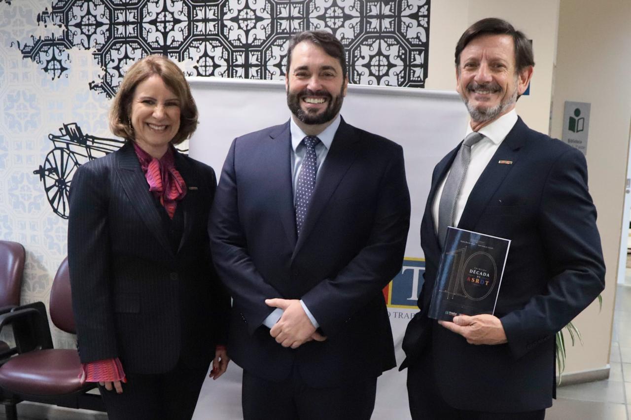 Os três posam para a foto sorrindo. André segura um exemplar do livro. 