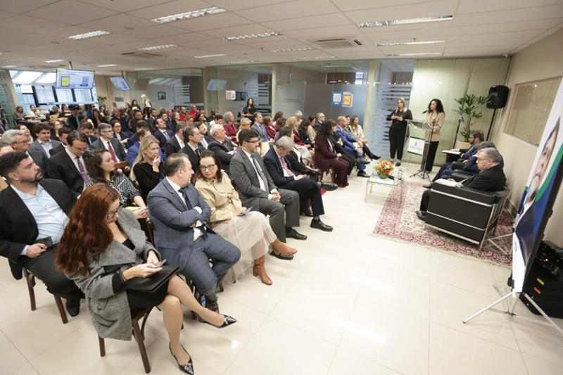 A foto mostra, de lado, a plateia e os palestrantes.