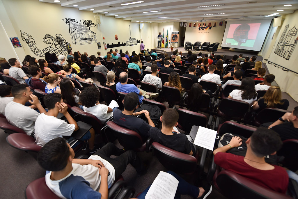 Auditório da escola judicial com grande presença de público. ao fundo aparece o mestre de cerimônias no palco e a arte do evento.
