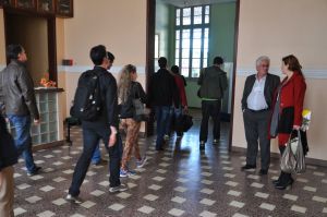 Sete pessoas de costas entram em uma sala de aulas. Na direita duas pessoas conversam.