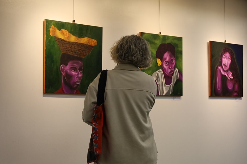 A imagem mostra uma mulher de costas observando as obras.
