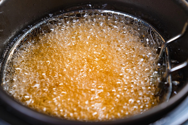 A fotografia mostra uma fritadeira cheia de óleo quente borbulhante e amarelado.