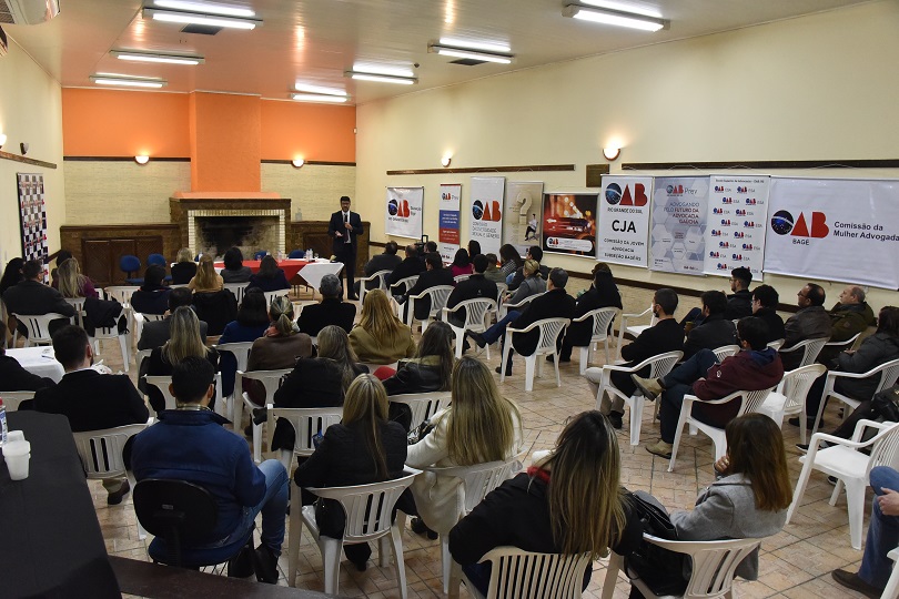 Foto em ângulo aberto do evento, mostrando público e o des. Rossal, em pé
