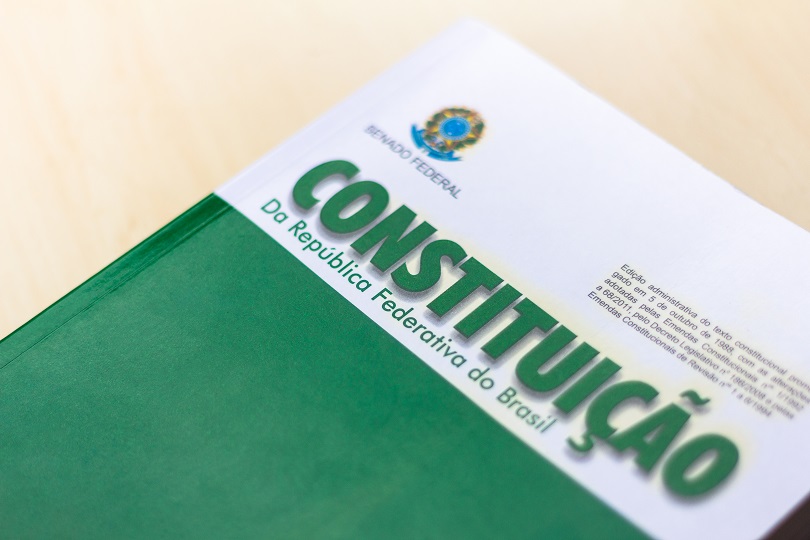 Foto ilustrativa mostra a capa de uma Constituição Federal, nas cores branca e verde, com um brasão da República.