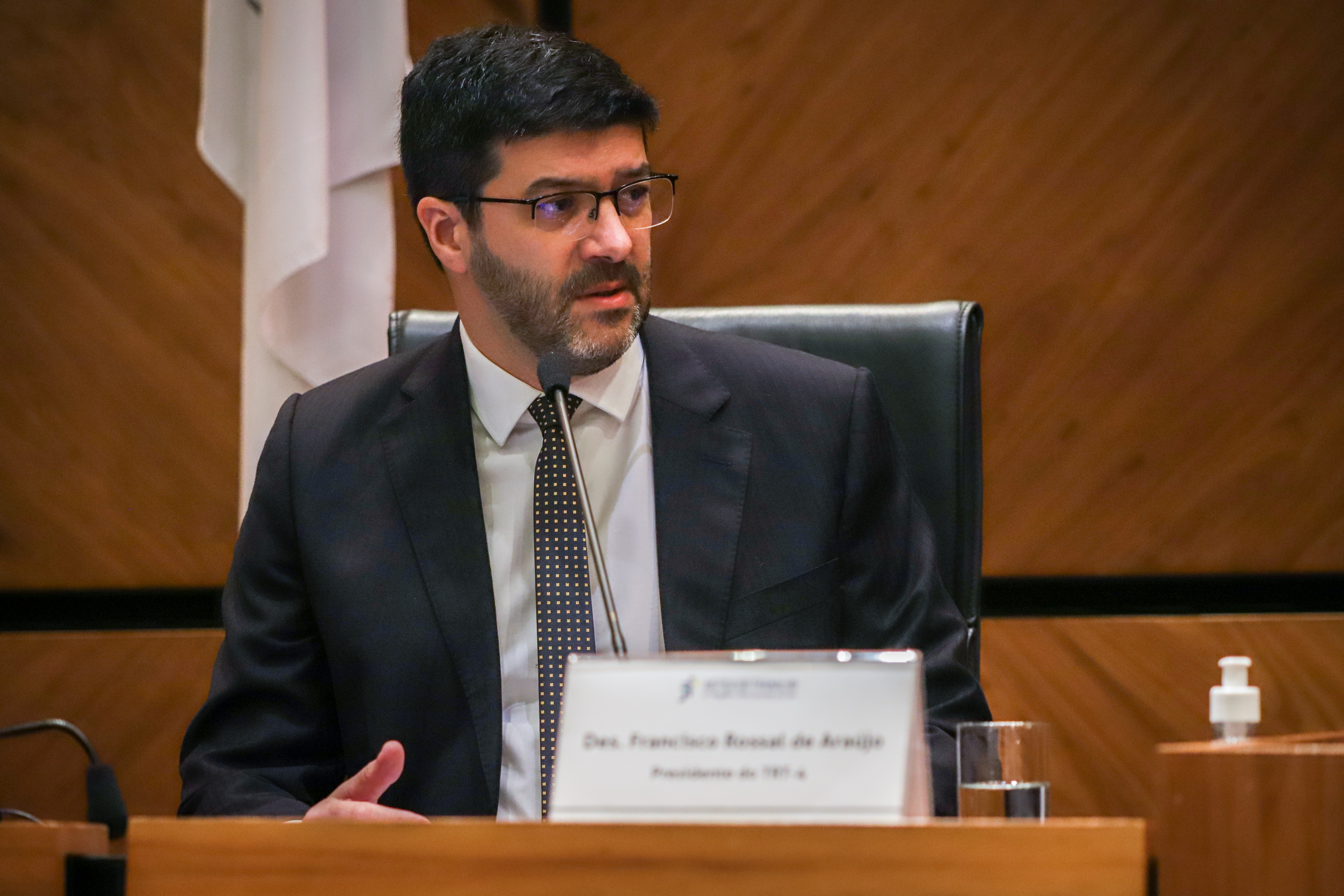 Francisco Rossal é branco, usa óculos, cabelo escuro e barba curta. Fala ao microfone. 