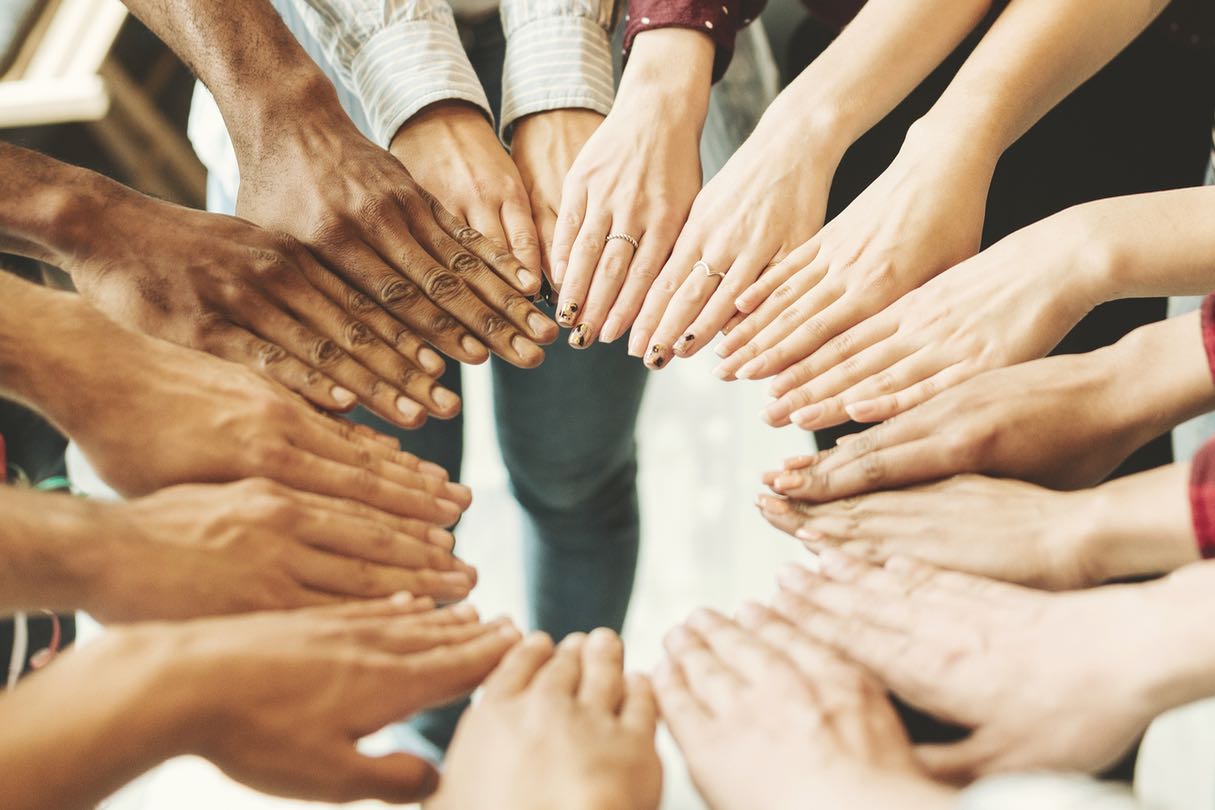 Foto das mãos de várias pessoas formando um círculo, representando a união de esforços para atingir um objetivo comum.