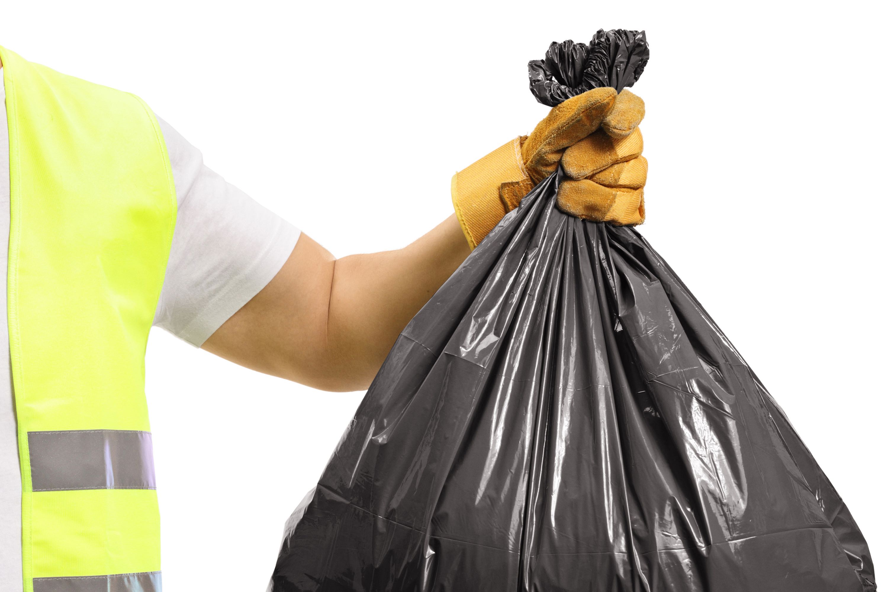 braço de um homem usando colete amarelo, luva e segurando um saco de lixo. 